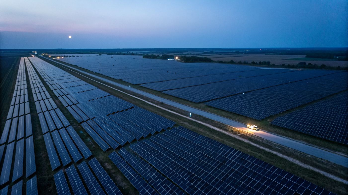 Aerial view of massive solar farm at dusk, geometric panels stretching to horizon bisected by a single road
